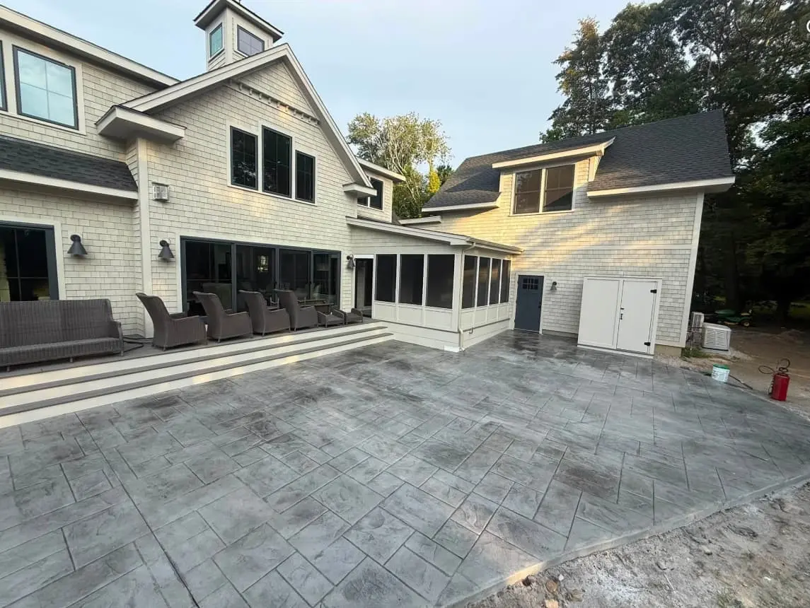 A large ashlar-pattern stamped concrete patio behind a shingled home