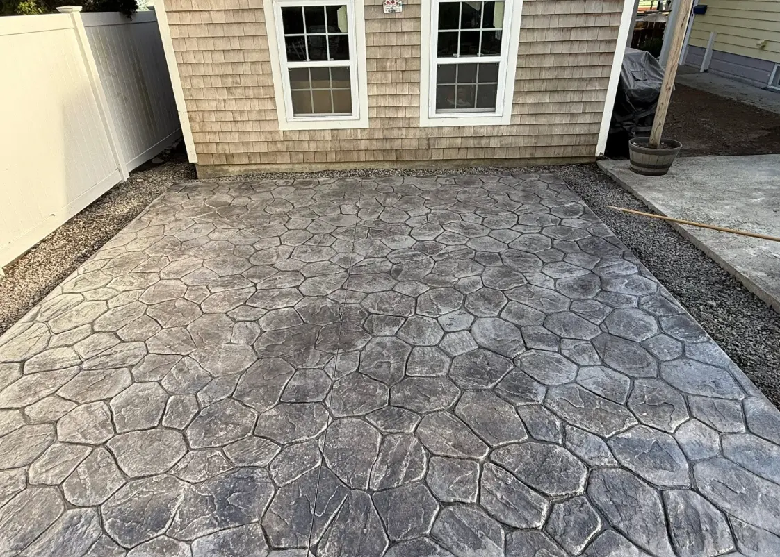 Grey stamped concrete patio with a cobblestone pattern beside a shingled house